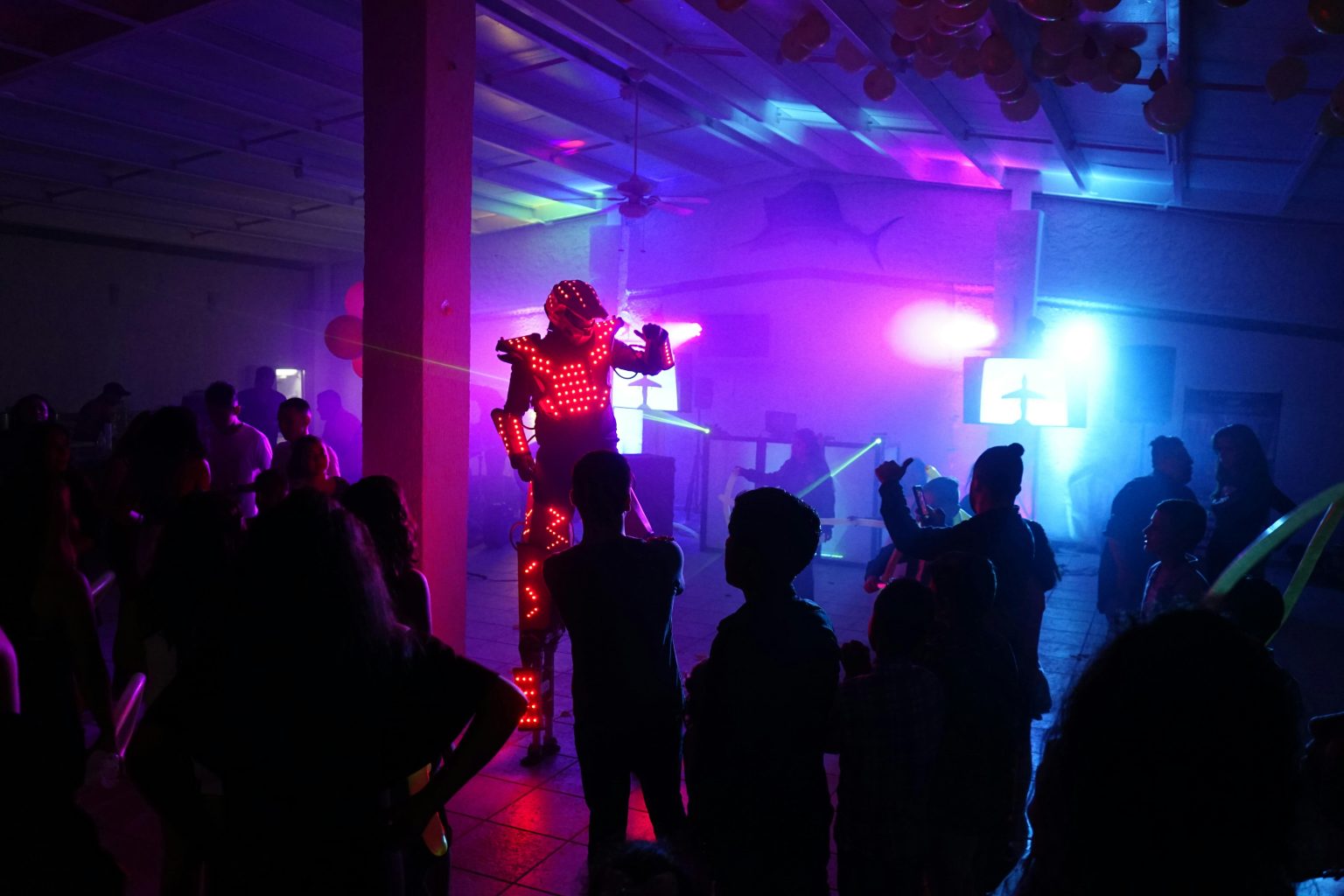 LED robot entertaining crowd with colorful lights at an indoor party.